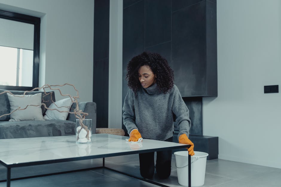 A woman wearing gloves cleans a table in a contemporary living room setting.